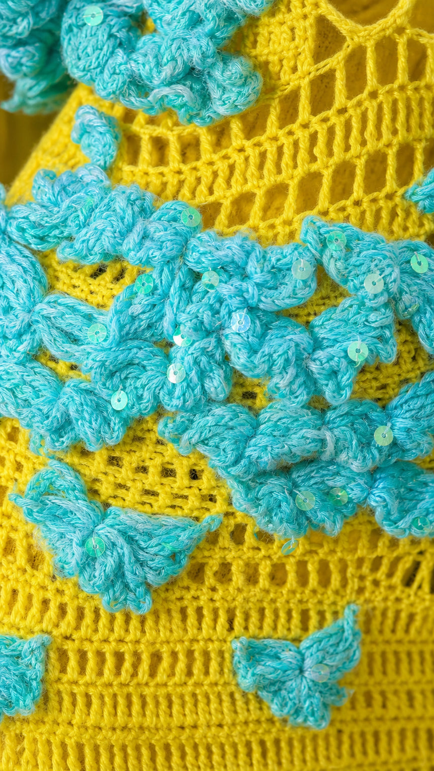 Close-up detail of turquoise 3D floral crochet appliques with clear sequins on yellow knit fabric