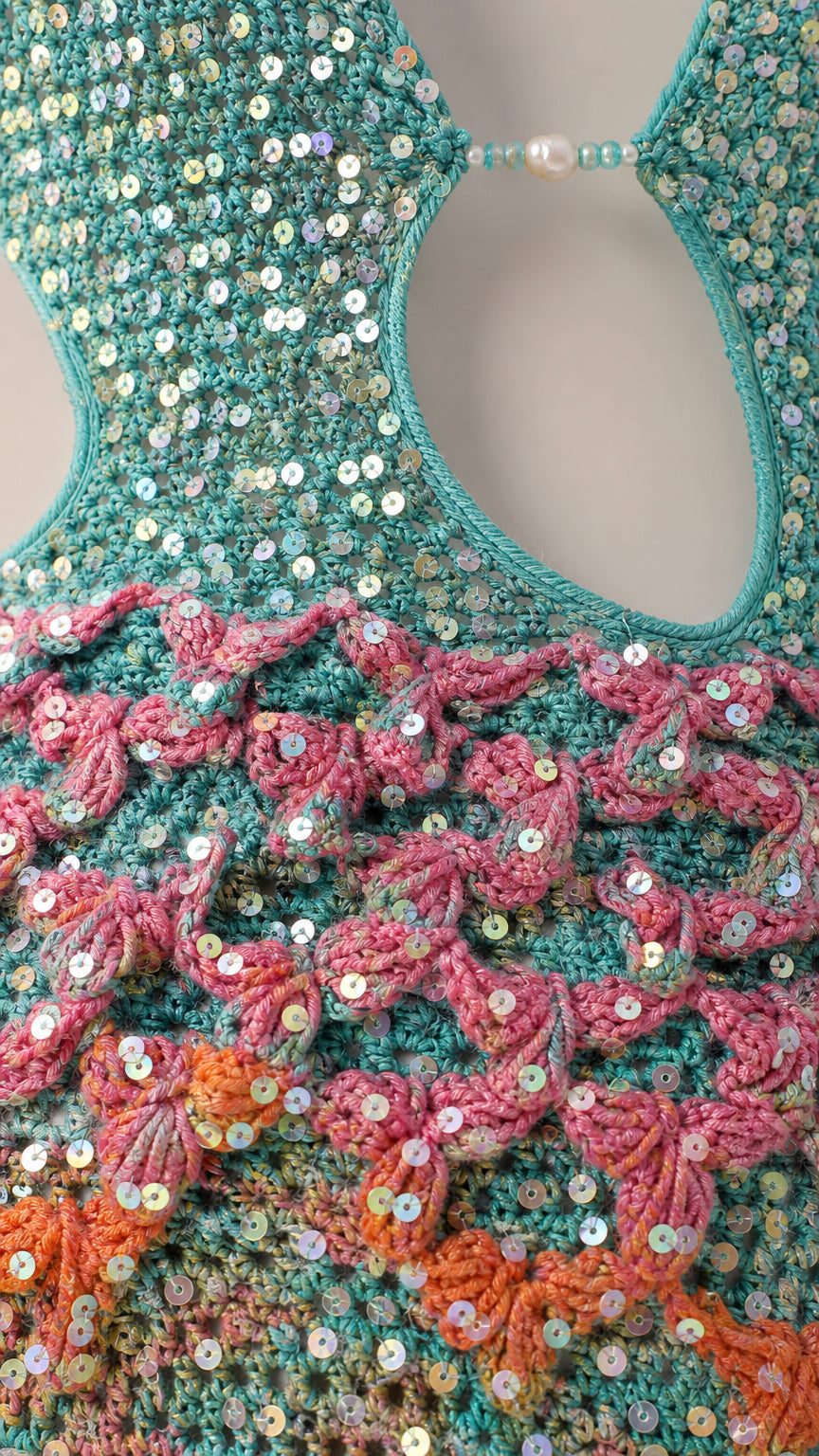 Close-up detail of turquoise sequin crochet knit, scalloped stitching, and center pearl bead connector